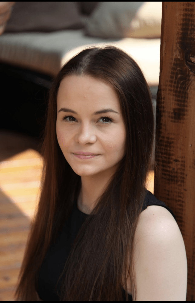 Woman with long brown hair leaning against a wooden post.