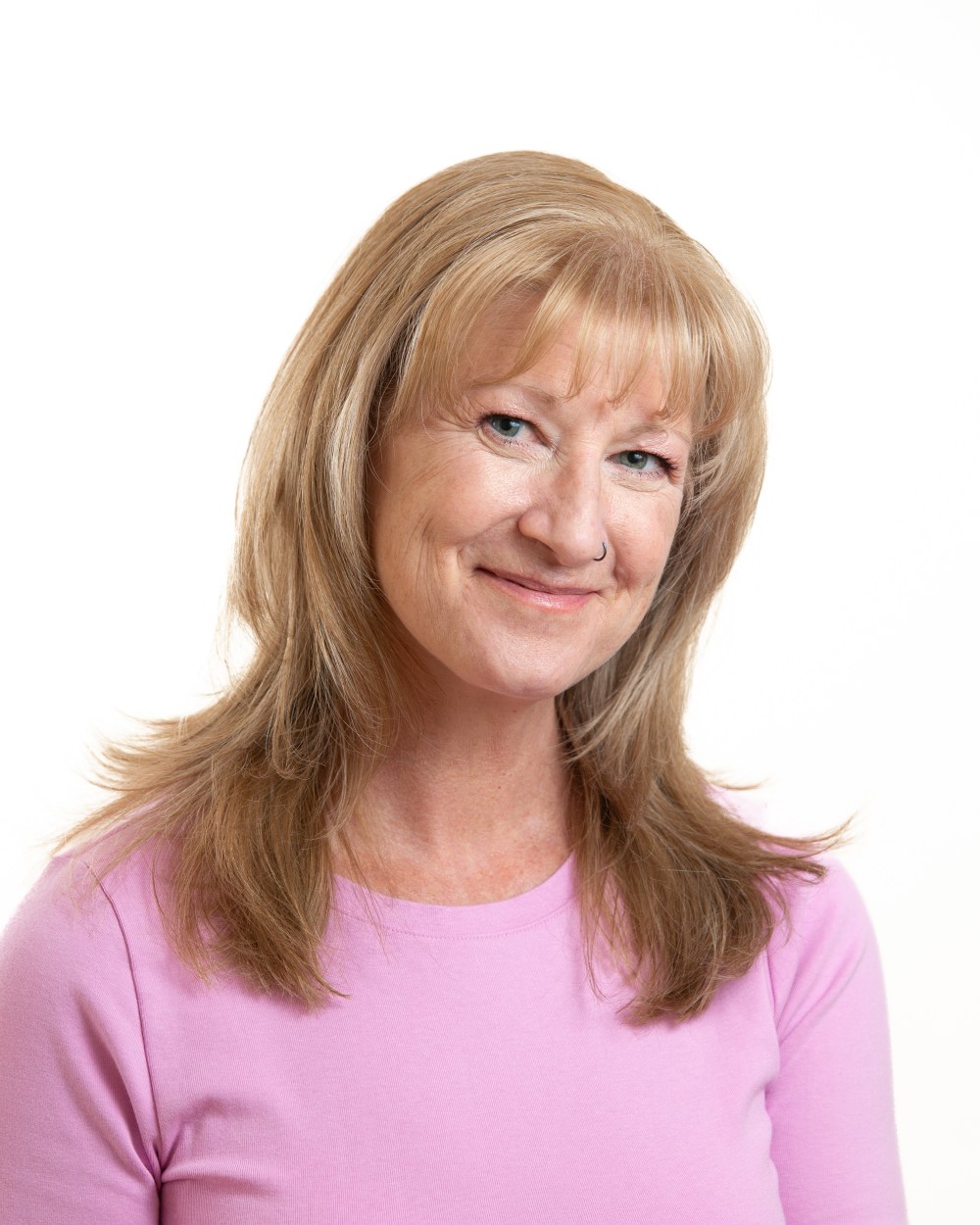 Smiling woman with long hair and pink shirt against white background.