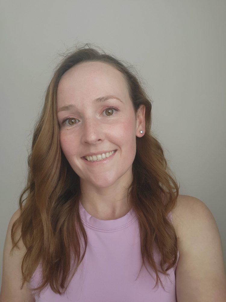 Smiling person with long hair wearing a pink top against a plain background.