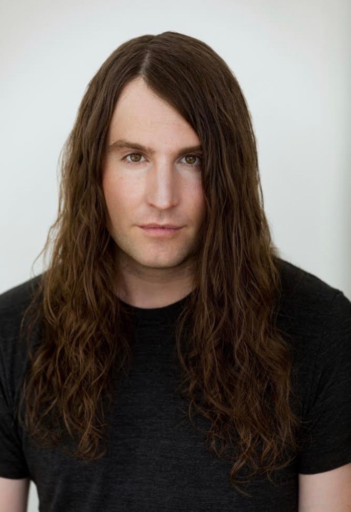 Person with long brown hair wearing a black shirt, facing the camera.