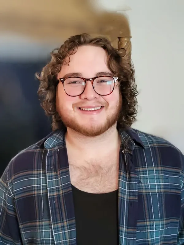 Michael Headshot Smiling person with curly hair and glasses wearing a plaid shirt indoors.