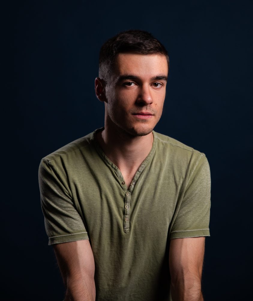 Man in green shirt against dark blue background, looking slightly to the side.